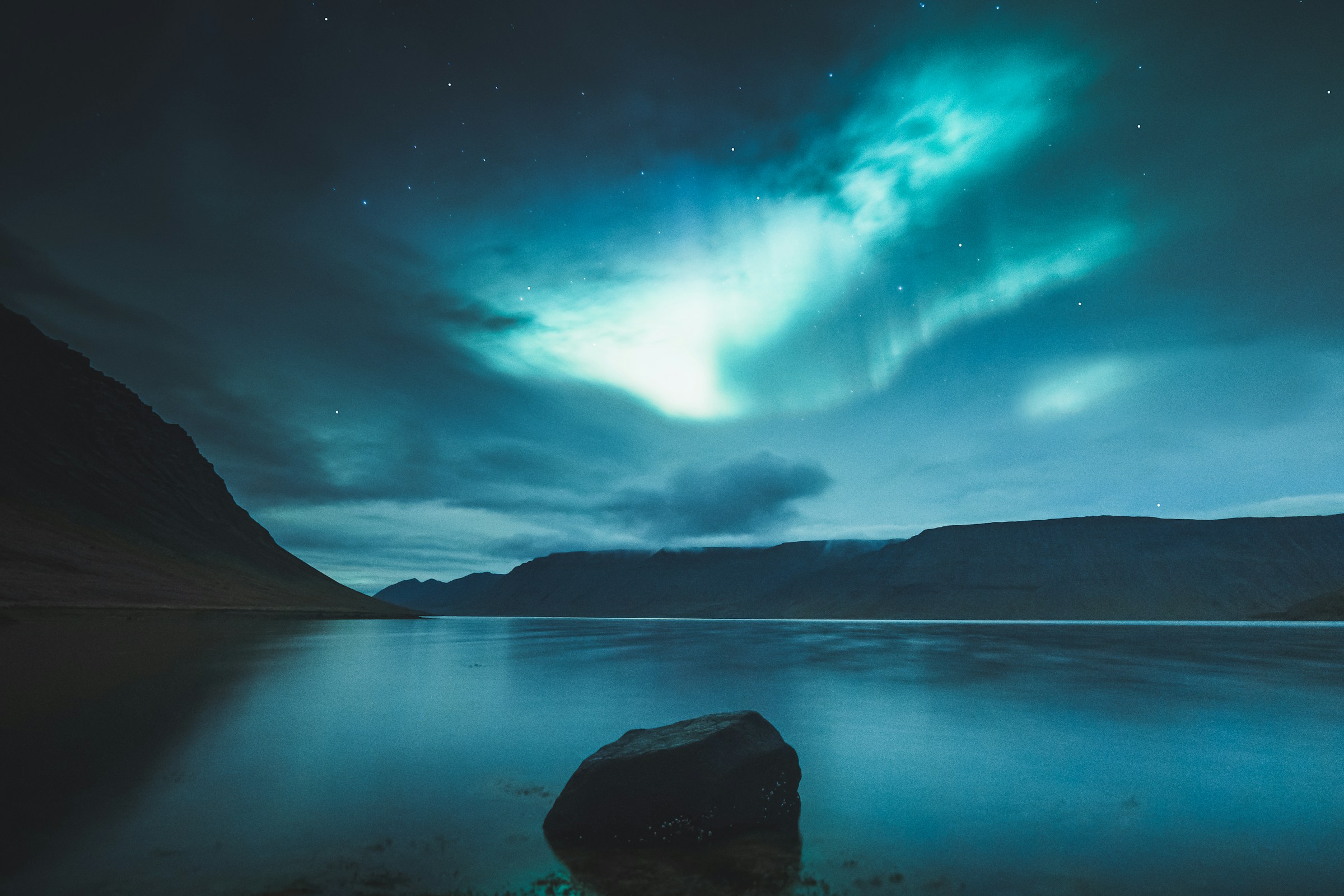 Turquoise aurora over a lake and mountains at night