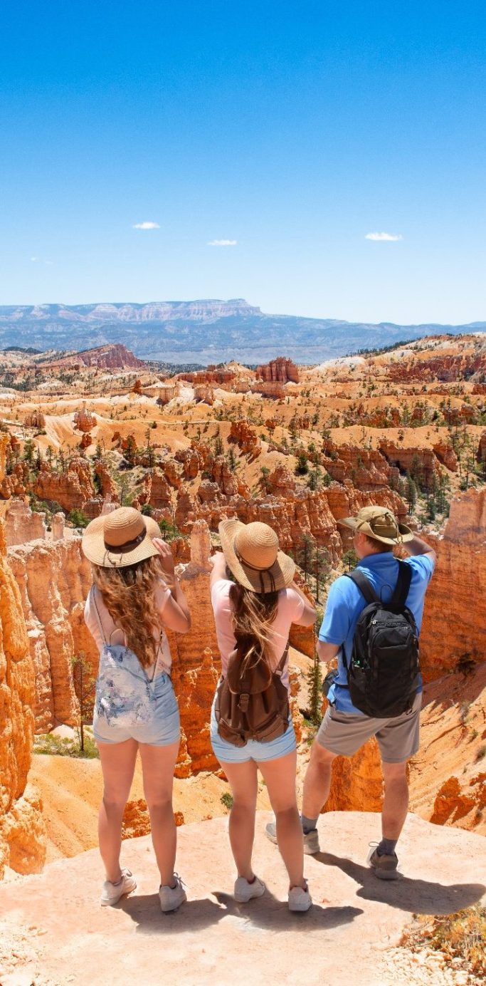 Trois personnes admirant un paysage de canyon sous un ciel bleu dégagé.